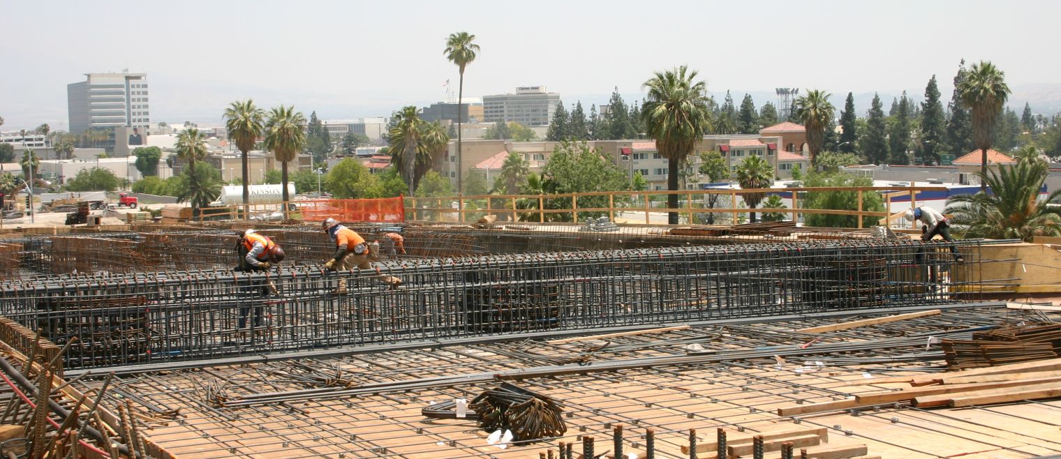 workers installing rebar on the bridge with palm trees and buildings in the background