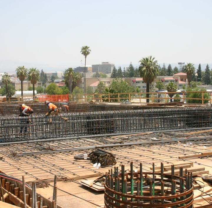 workers installing rebar on the bridge with palm trees and buildings in the background